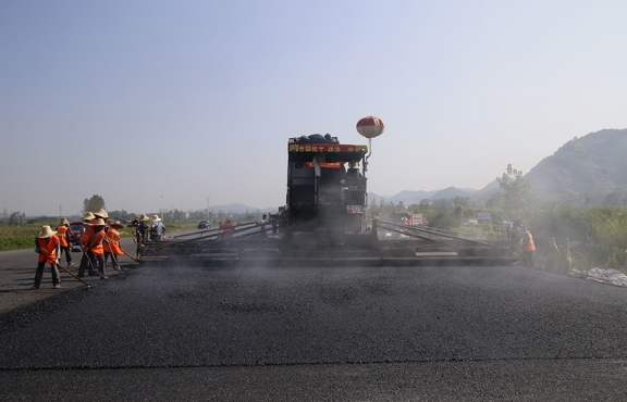 2019年8月，宜春經(jīng)開(kāi)區(qū)S311路面攤鋪現(xiàn)場(chǎng)，工友們輔助路面兩側(cè)的分料、補(bǔ)窩等作業(yè)